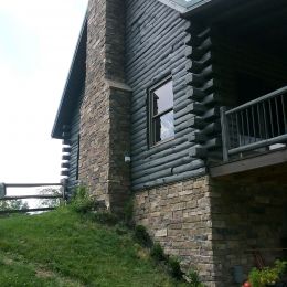 Log Home with a Gray Stain and Stone Covered Foundation