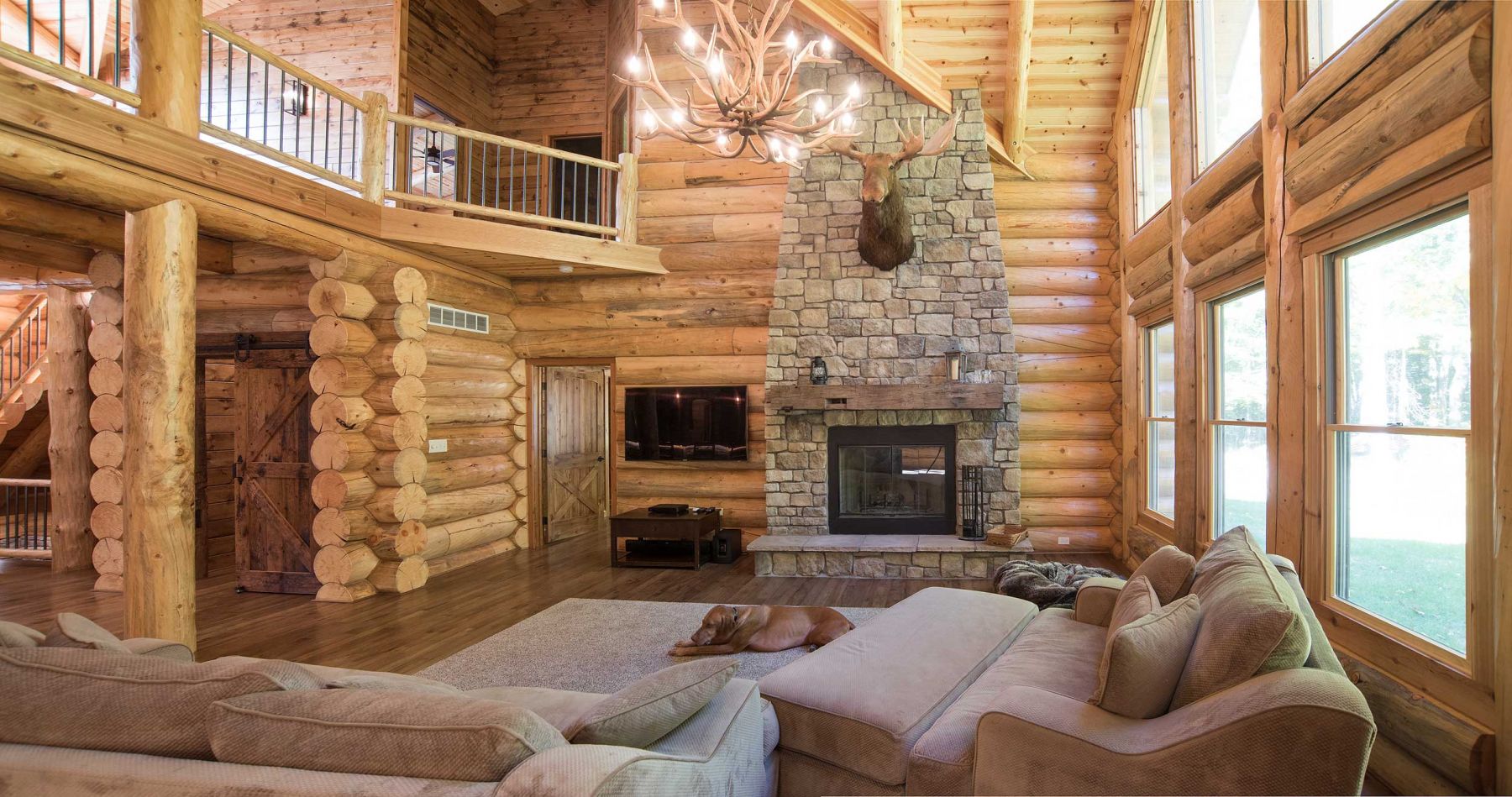 Log home great room with floor to ceiling fireplace and large antler chandelier 